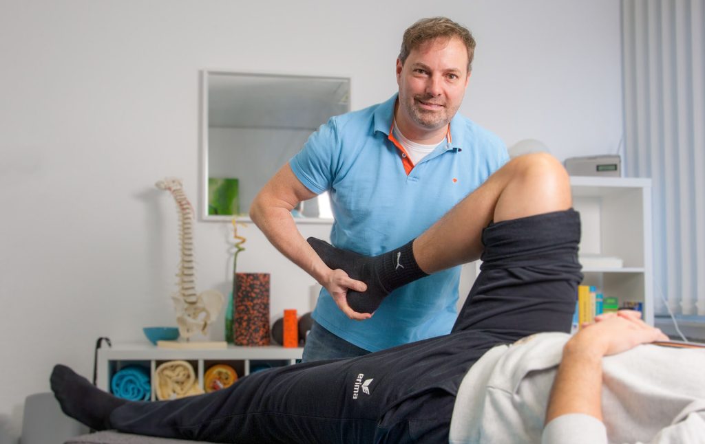 Physiotherapeut Frank Pawlitschko mobilisiert das Bein eines Patienten.